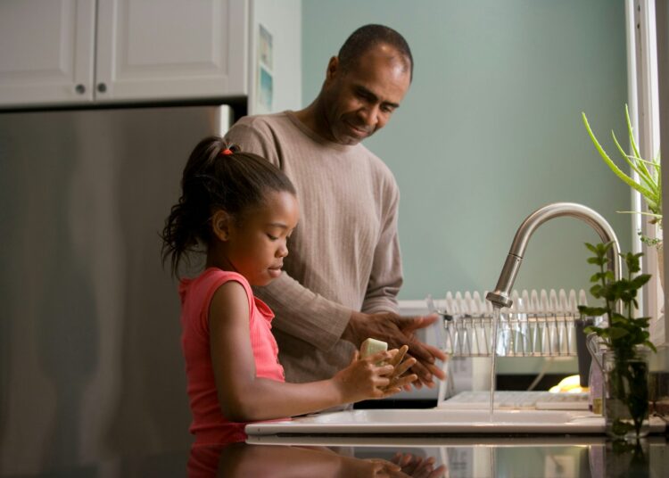 man in long sleeve shirt standing beside girl in pink tank top washing hands