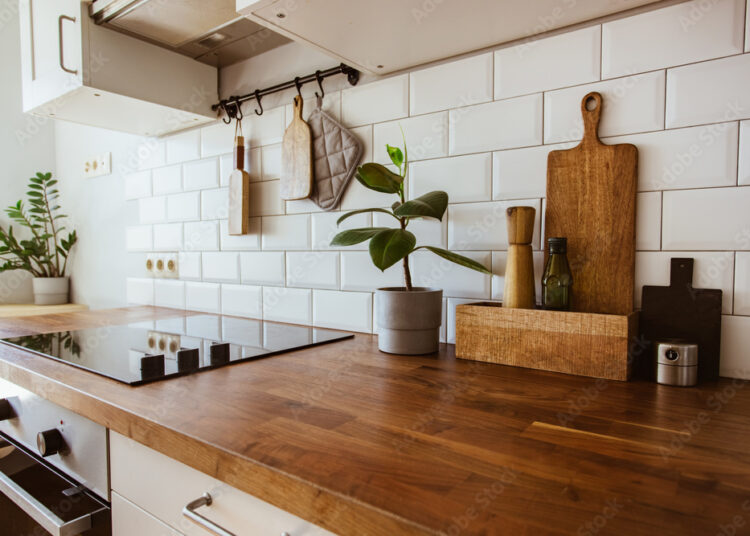 Kitchen brass utensils, chef accessories. Hanging kitchen with white tiles wall and wood tabletop.Green plant on kitchen background